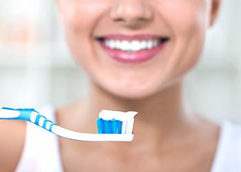 Woman smiling holding a toothbrush with toothpaste