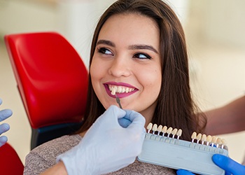 Woman smiling sitting in dental chair while shade of teeth are matched with dental shade-guide